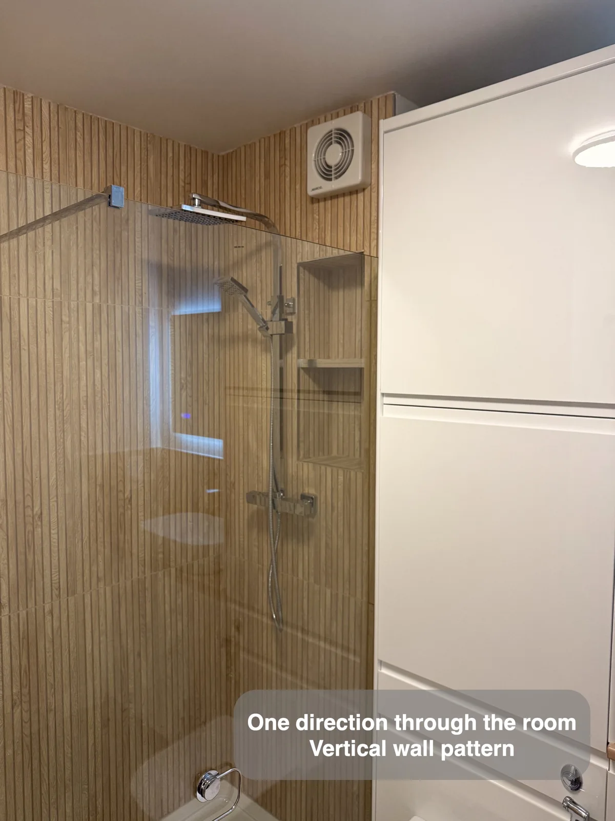 Shower glass and chrome fittings against a vertical wood-effect wall.