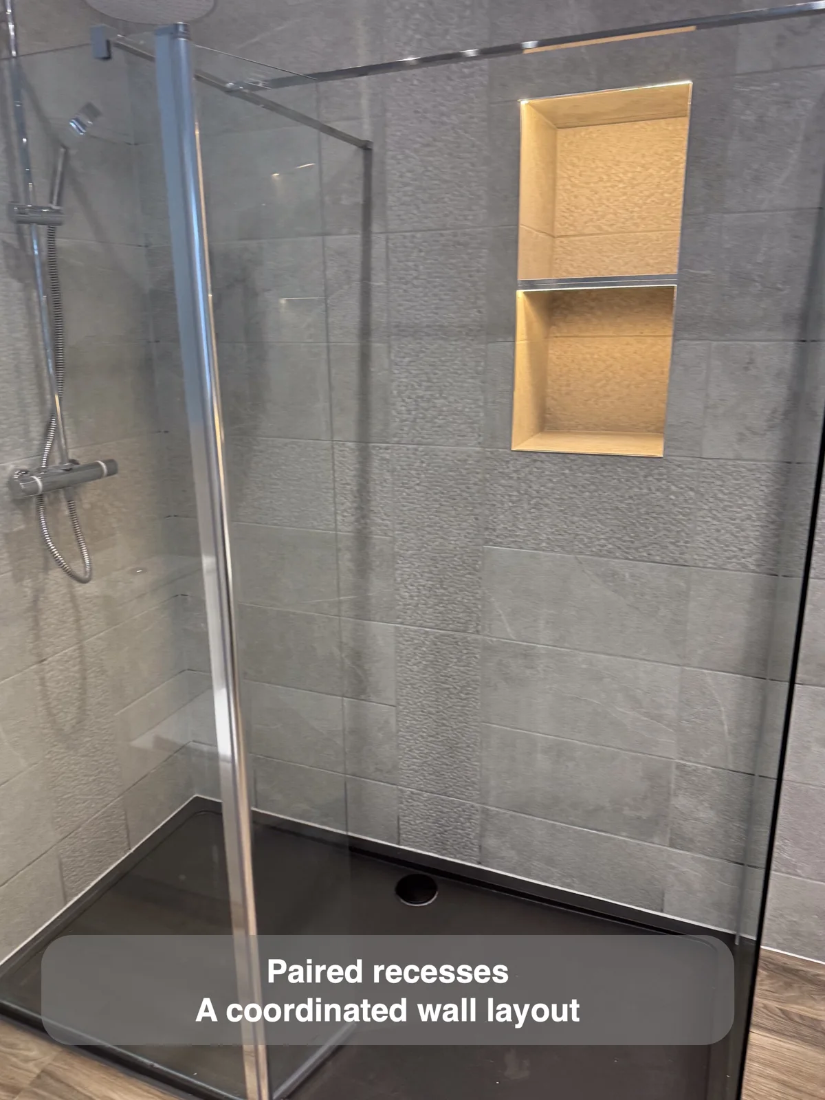Two warm illuminated recesses arranged vertically in a grey tiled shower.