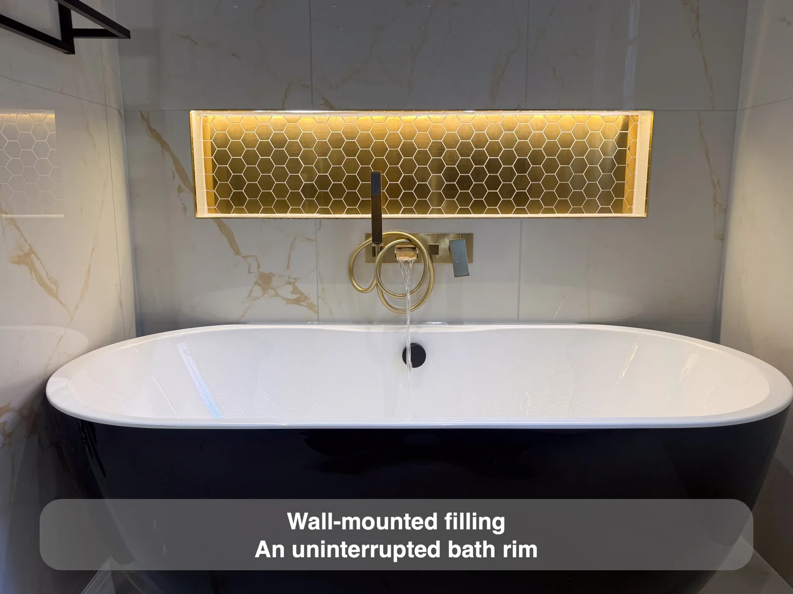 Brass wall filler/handset above freestanding black-shell white-rim bath, mosaic recess.