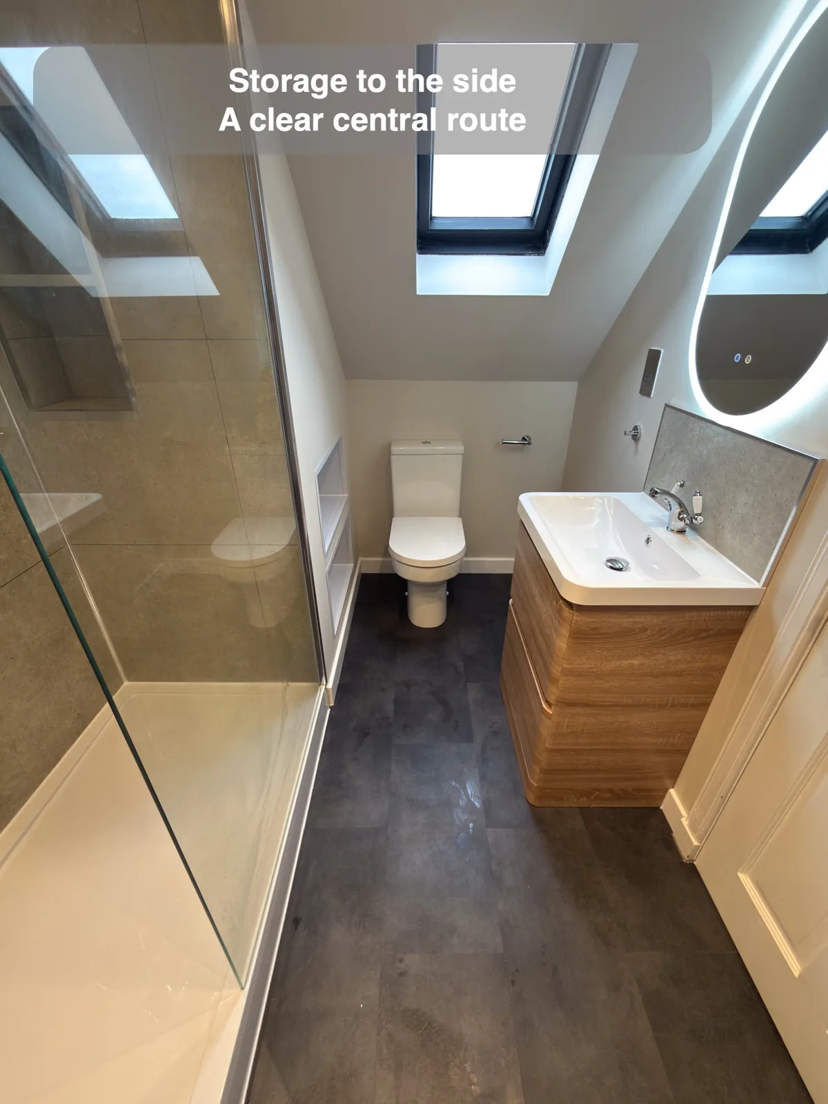 Compact timber vanity opposite glass shower with floor route to toilet under rooflight.