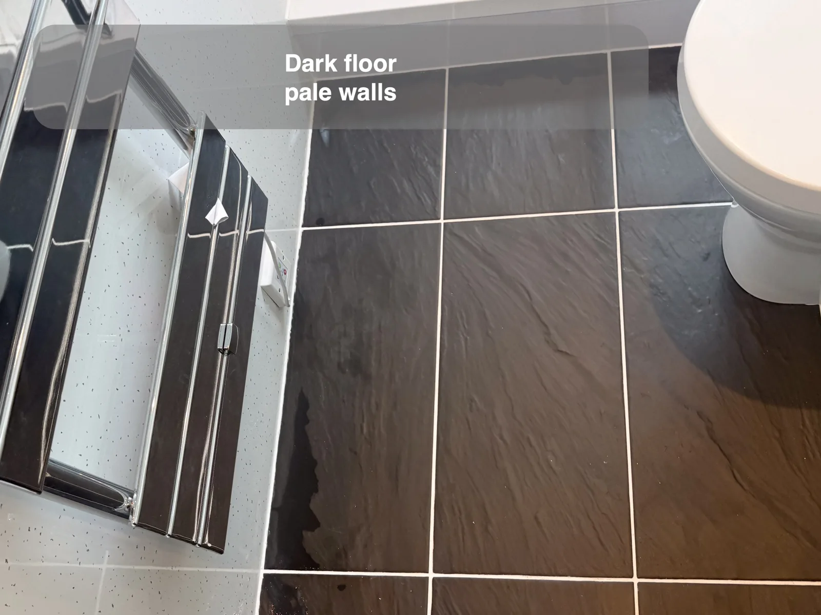 Dark rectangular stone-effect floor tiles with pale joints beside pale speckled walls, a chrome radiator and white toilet.