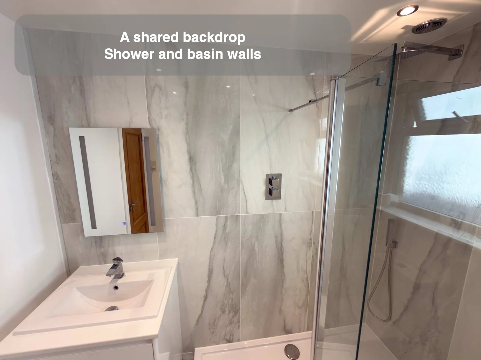 Pale vertically marked walls beside a shower, basin and toilet.