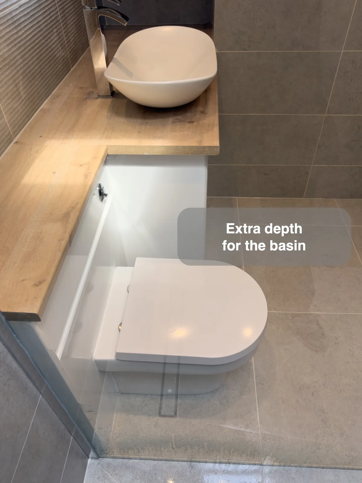 White vessel basin on a deeper timber-effect worktop beside a shallower matching ledge over a white toilet.