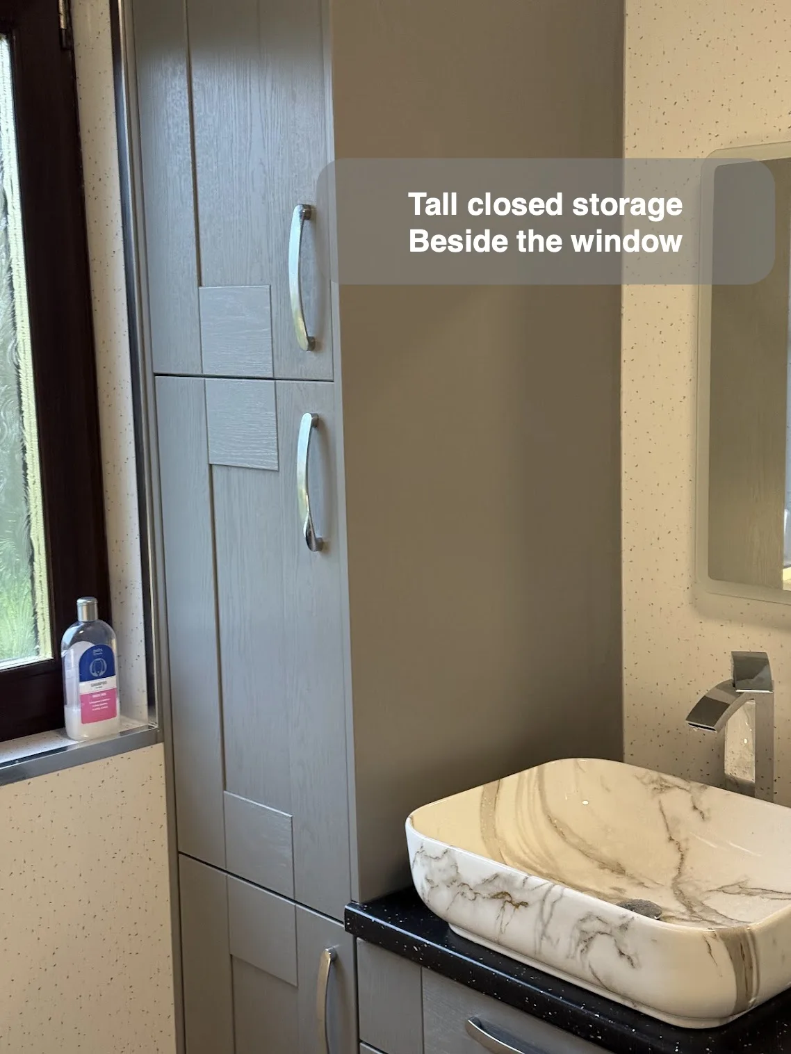 Tall grey cabinet beside window and stone-pattern vessel basin on dark worktop.