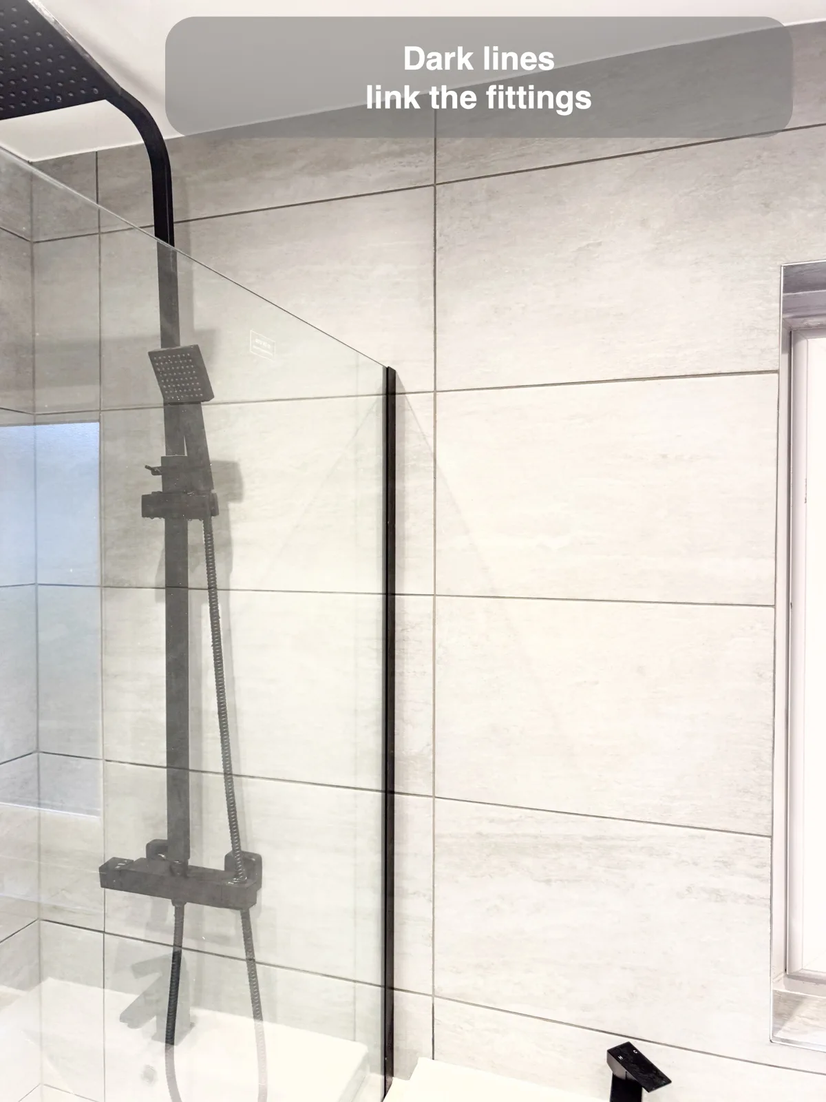 Black shower rail and glass edge against pale grey walls with dark rectangular joint lines.