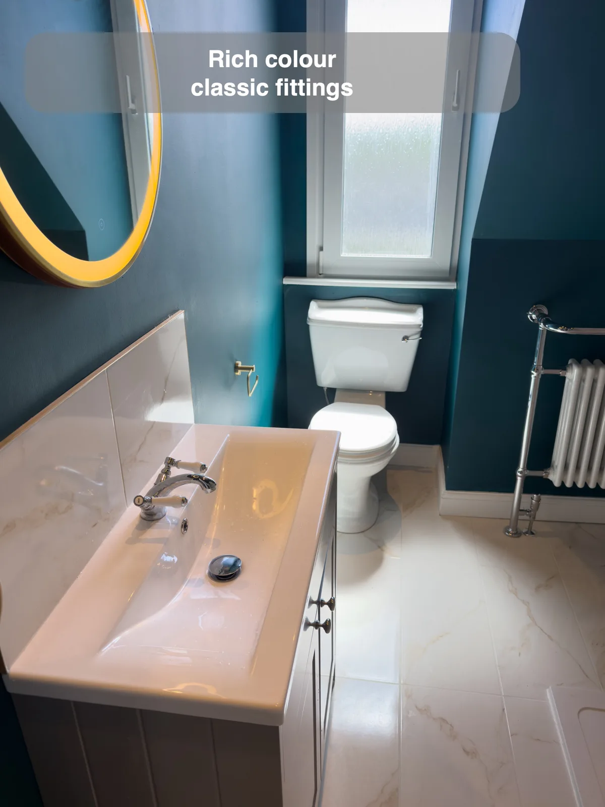 Teal painted walls around a white toilet with lever flush, traditional chrome basin tap and column radiator.